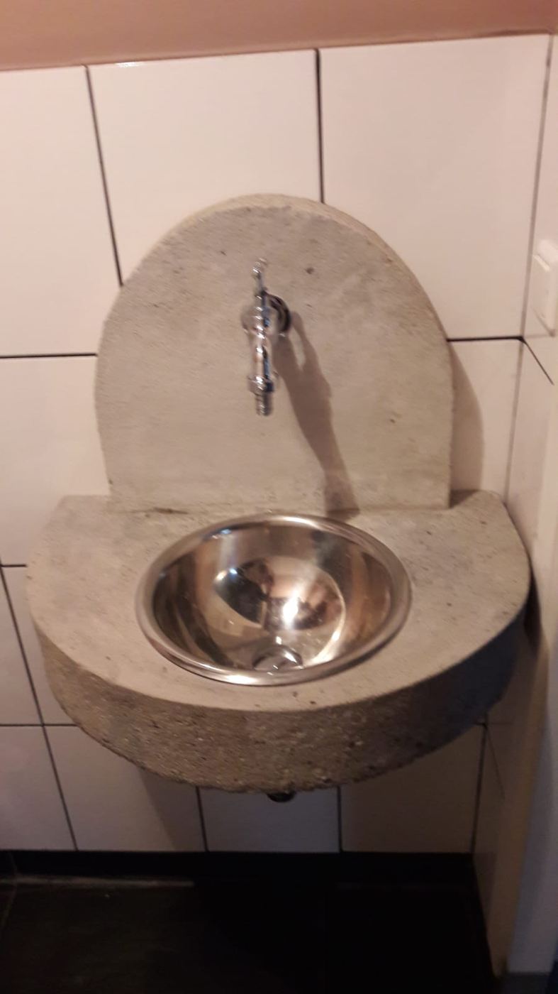 Wastafel van beton met rvs kom tegen een wit betegelde wand