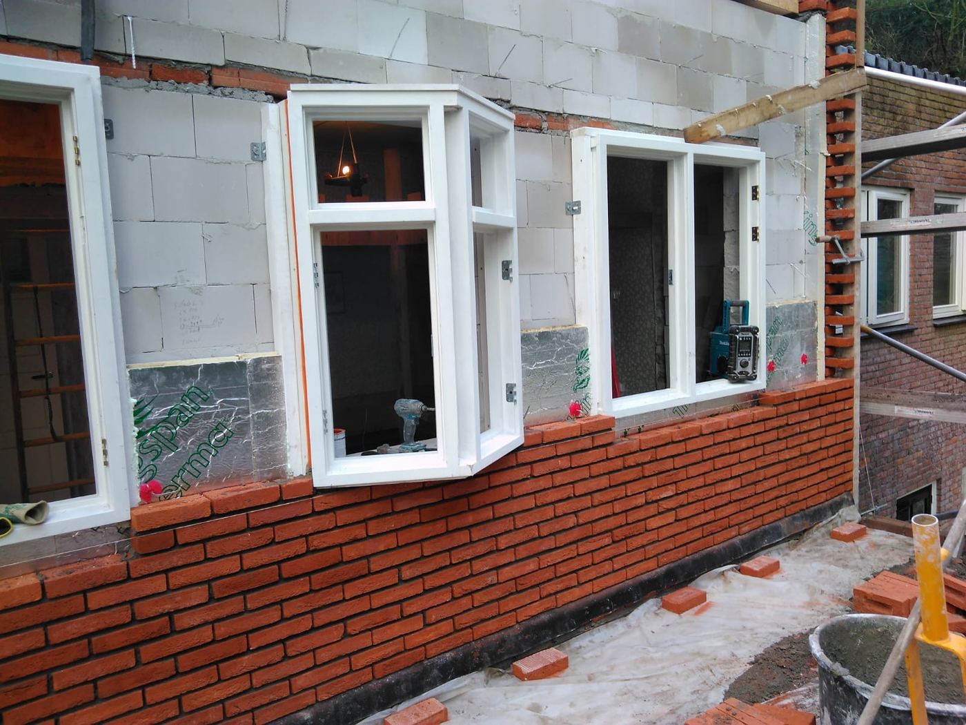 Nieuw metselwerk met witte kozijnen en erker tijdens een renovatie